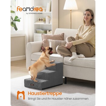 Hellbraune Französische Bulldogge klettert graue Haustiertreppe auf ein Sofa mit einer sitzenden Frau; sichtbarer Text ‚feandrea by SONGMICS HOME‘ und ‚Haustiertreppe‘.