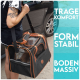 Eine tätowierte Person trägt eine schwarze und orangefarbene Tragetasche für Haustiere mit Netzpaneelen und Text: "TRAGE KOMFORT," "FORM STABIL," "BODEN MASSIV."