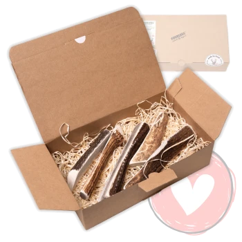 Offene Kraft-Geschenkbox mit Papierstreu und mehreren halbierten Geweih-Kausnacks; Deckel zeigt 'FOURLEGS'.