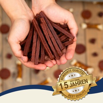 Hände halten einen Stapel Hundeleckerlis, mit einem Abzeichen, das "Beste Qualität - seit über 15 Jahren" auf einem Holz-Hintergrund zeigt.