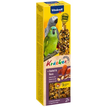 Vitakraft Kräcker vogeltraktatie doos met twee stokken van dadels en noten, met een groene en grijze papegaai en info over vitamines en mineralen.