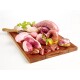 Ein Holzschneidebrett zeigt verschiedene rohe Fleischsorten, darunter Hähnchen, Schweinefleisch und Innereien, garniert mit frischen Kräutern und einer kleinen Schüssel Öl.