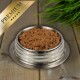 Eine Edelstahlschüssel für Haustierfutter, gefüllt mit hochwertigem Nassfutter für Katzen, auf einer Holzoberfläche mit grünem Gras im Hintergrund.