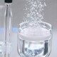 Ein Glas, das mit klarem Wasser gefüllt ist und sprudelt, während Gas aus einem Rohr darüber freigesetzt wird, wodurch eine schaumige Oberfläche entsteht.