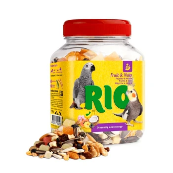 Ein klares Glas mit RIO Fruit & Nuts Vogelfutter, mit bunten Samen und Nüssen, die herausfallen, mit Bildern eines grauen Papageis und eines Nymphensittichs auf dem Etikett.