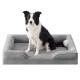 Schwarz-weißer Border Collie sitzt auf einem grauen, plüschigen Hundebett mit Randpolstern.