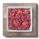 Ein quadratisches weißes Geschirr, gefüllt mit rohem Hackfleisch, das eine Mischung aus roten und rosa Farbtönen zeigt, auf einer Holzoberfläche platziert.