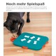 Ein schwarzer Hund interagiert mit einem türkisfarbenen Puzzlespielzeug mit weißen, knochenförmigen Teilen, entworfen für fortgeschrittenes Spielen, um versteckte Leckereien zu finden.
