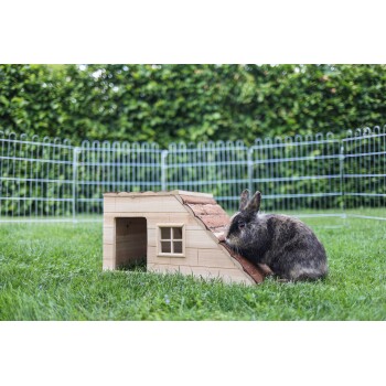 Ein brauner und grauer Kaninchen sitzt neben einem Holzkaninchenhaus mit einem schrägen Dach und einem kleinen Fenster, auf grünem Gras.
