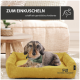 Ein gemütlicher Hund in einem grünen Halstuch ruht auf einem gelben Bett mit weichen Möbeln im Hintergrund. Text: "ZUM EINKUSCHELN schafft ein gemütliches Ambiente."