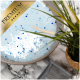 Eine Schüssel mit blauen und weißen Haustierbadesalzen mit einem goldenen 'PREMIUM'-Label, umgeben von einer kleinen Topfpflanze und einem grauen Haustierpflegewerkzeug.