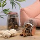 Zwei Glasbehälter, gefüllt mit Leckerlis für Haustiere, einer umgekippt, neben einem gewundenen Seilspielzeug auf einem Holztisch, mit einem rosa Sofa im Hintergrund.