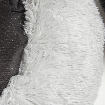 Nahaufnahme eines weichen, flauschigen Haustierbettes mit einem weißen, plüschigen Äußeren und einem schwarzen gepunkteten Inneren.