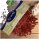 Eine Tüte mit Haustierleckerlis, die kleine, rote, würfelförmige Stücke auf eine Holzoberfläche fallen lässt, mit einem teilweise sichtbaren Seilspielzeug.