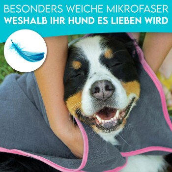 Ein glücklicher Hund in einem grauen Handtuch mit pinkem Rand, von einer Person gekuschelt. Text: "Besonders weiche Mikrofasern, weshalb Ihr Hund es lieben wird."