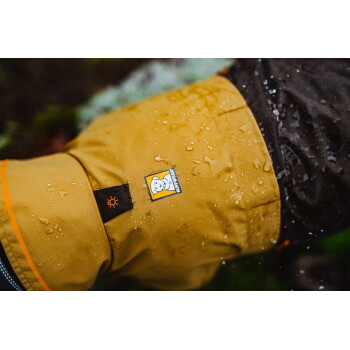 Eine Nahaufnahme einer wasserdichten Hundejacke in Gelb mit Wassertropfen, die ein Ruffwear-Logo und ein Sonnensymbol auf dem Ärmel zeigt.