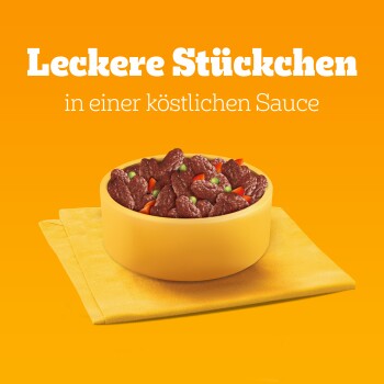 Schüssel mit Haustierfutter mit Stücken in einer herzhaften Sauce, mit Erbsen und roten Paprika, auf einer gelben Serviette vor einem orangefarbenen Hintergrund.