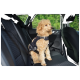 A fluffy, light-colored dog wearing a black harness sits in the back seat of a car, secured with a seatbelt.