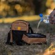 Braun-schwarze Reisetasche für Haustiere mit zusammenklappbarer Wasserschüssel, die auf dem Gras aus einer Plastikflasche befüllt wird.