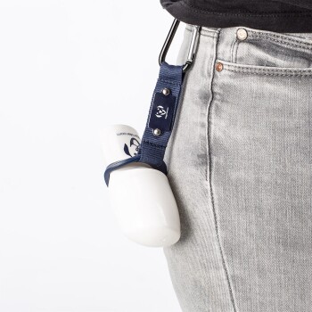 Eine Person in Shorts hält eine Haustier-Wasserflasche an den Mund eines Hundes, während der Hund eifrig daran leckt. Die Szene spielt sich in einem grasbewachsenen Bereich ab.