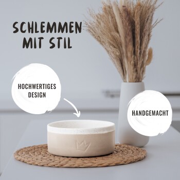 Eine handgefertigte Haustierschale auf einem geflochtenen Platzdeckchen neben einer Vase mit getrockneten Blumen. Text: "Schlemmen mit Stil," "Hochwertiges Design," "Handgemacht."