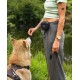 Eine Frau in einem grün gestreiften Crop-Top und grauen Hosen steht im Freien mit einem braun-weißen Shiba Inu an der Leine.
