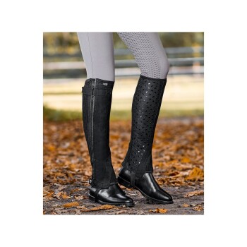 Eine Nahaufnahme einer Person, die stilvolle schwarze Reitstiefel mit strukturiertem Design trägt und auf einem mit Herbstblättern bedeckten Boden steht.