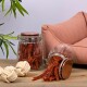 Zwei Glasbehälter gefüllt mit Haustierleckereien, einer umgekippt und verschüttet Leckereien, neben einem Seilspielzeug, mit einem rosa Sofa im Hintergrund.