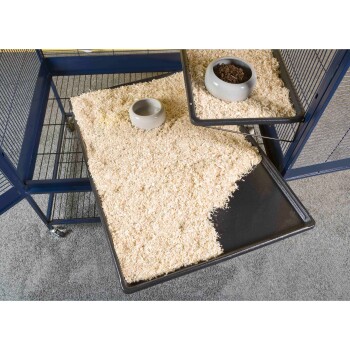 Ein Haustierkäfig-Tablett gefüllt mit Holzspänen, mit zwei grauen Futternäpfen, einem leeren und einem mit trockenem Haustierfutter.