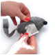 Une personne avec du vernis à ongles rouge tient un jouet en peluche gris en forme de souris, révélant un compartiment caché avec un coussinet en coton à l'intérieur.