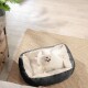 Ein flauschiger weißer Pomeranian sitzt glücklich in einem gemütlichen schwarzen Haustierbett mit einem weichen cremefarbenen Innenraum auf einem gewebten Teppich in einem hellen Raum.