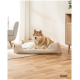 Ein gemütliches beiges Hundebett mit einem weichen Kissen, belegt von einem Hund, in einem hellen, modernen Wohnzimmer mit Holzboden und einer Pflanze.