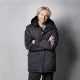Eine Person in einer schwarzen Winterjacke mit Kapuze, die mit verschränkten Armen vor einem grauen Hintergrund steht.