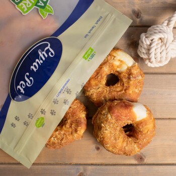 Eine Tüte mit Haustierleckereien, die mit "Premium Qualität" beschriftet ist, mit drei runden, knusprigen Hundesnacks auf einer Holzoberfläche, neben einem Seilspielzeug.