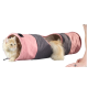 Een fluffy oranje kat die uit een roze en grijs gestreepte stoffen tunnel kijkt, met een menselijke hand in de buurt.