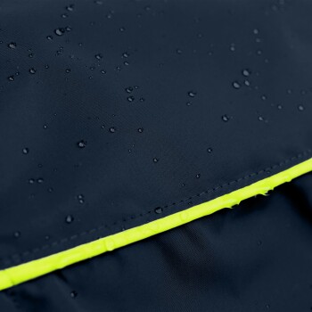 Ein brauner Hund trägt einen stilvollen schwarzen Regenmantel mit Kapuze und steht elegant neben einer Steinstruktur in einer städtischen Umgebung.