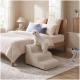 Kleiner weißer, flauschiger Hund auf beige gerippten Haustiertreppen neben einem Holz-Bett in einem hellen, neutralen Schlafzimmer.