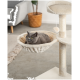 Eine graue Katze mit gelben Augen, die in einer gemütlichen, cremefarbenen Hängematte, die an einem Katzenbaum befestigt ist, entspannt, mit einem weichen Ball, der in der Nähe hängt.