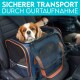 Ein Cavalier King Charles Spaniel sitzt in einer mit Sicherheitsgurt gesicherten Transportbox im Auto. Der Text darüber sagt "SICHERER TRANSPORT DURCH GURTAUFNAHME."