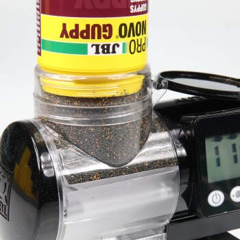Nahaufnahme eines gelb-roten Haustierfutterspenders mit der Aufschrift "Pro Novo Guppy" mit schwarzen Granulaten und einem digitalen Display, das "111" anzeigt.