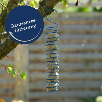 Ein blauer Spiral-Futterspender, der von einem Baumzweig hängt und mehrere Vogelfutterbälle hält, mit dem Text 'Ganzjahresfütterung' in einem kreisförmigen Design.