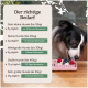 Fütterungsanleitung für Hunde nach Gewicht mit täglichen Grammangaben und Dauer, neben einem schwarz-weißen Hund, der aus einem rosa Slow Feeder frisst.