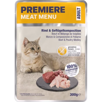 Eine hellbraune Katze sitzt neben einem Schieferplatte mit rohem Fleisch, mit einem Verpackungslabel, das 'Premiere Meat Menu' und 'Rind & Geflügel Medley' liest.