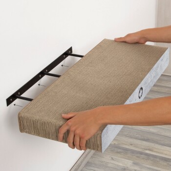 Eine Person installiert einen wandmontierten Kratzbaum für Katzen und hält die Kratzfläche, die aus strukturiertem Karton besteht, gegen eine Metallhalterung.