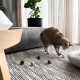 Eine verspielte getigerte Katze interagiert mit bunten Filzkugeln auf einem gemusterten Teppich in einem gemütlichen Wohnzimmer, mit einer Topfpflanze im Hintergrund.
