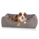 Ein glücklicher Australian Shepherd Hund, der in einem gemütlichen grauen Hundebett mit dem Logo 'KNUFFELWUFF' auf der Vorderseite entspannt.
