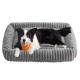 Schwarz-weißer Border Collie mit orangefarbener Bandana liegt auf einem grauen Plüsch-Haustierbett mit gerippter Struktur.