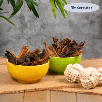 Zwei Schalen mit getrockneten Rindfleischsnacks in gelber und grüner Schale neben einem geknoteten Seilspielzeug auf Jute, Text ‚Rindereuter‘ sichtbar