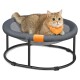 Eine flauschige Katze mit einem leuchtend orangefarbenen Halstuch ruht sich bequem auf einem runden, grauen Haustierbett mit einem Netzmittel und einem schwarzen Metallrahmen aus.