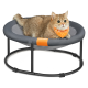 Eine flauschige Katze mit einem leuchtend orangefarbenen Halstuch ruht sich bequem auf einem runden, grauen Haustierbett mit einem Netzmittel und einem schwarzen Metallrahmen aus.
